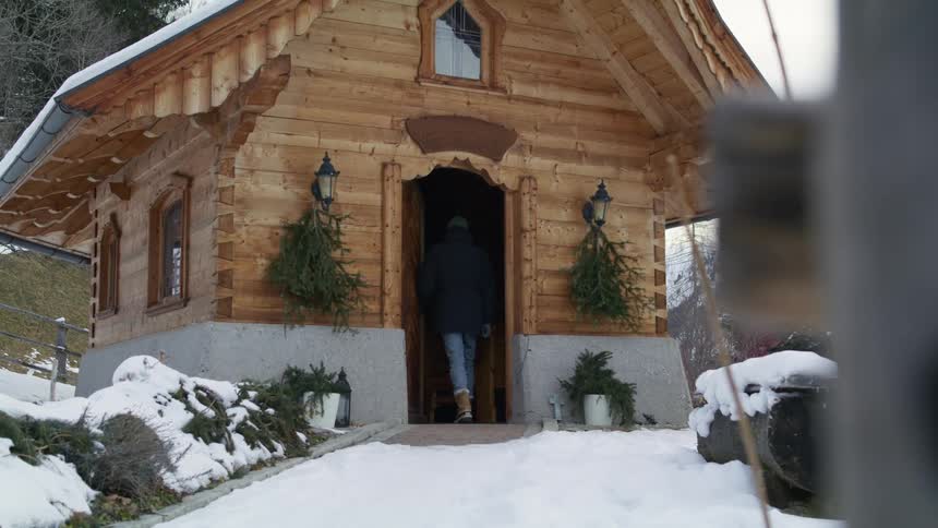 A person standing before a wood cabin on a winter day opens the cabin door and enters