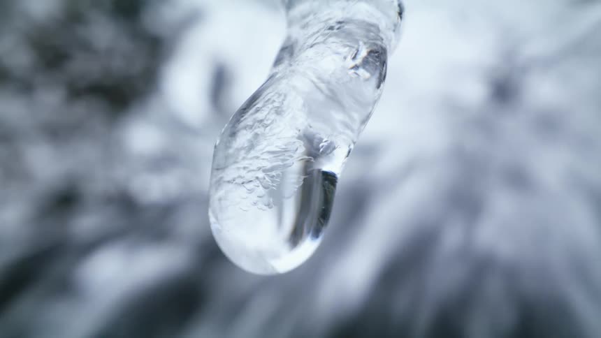 Water drop dripping from an icicle hanging near a waterfall at winter