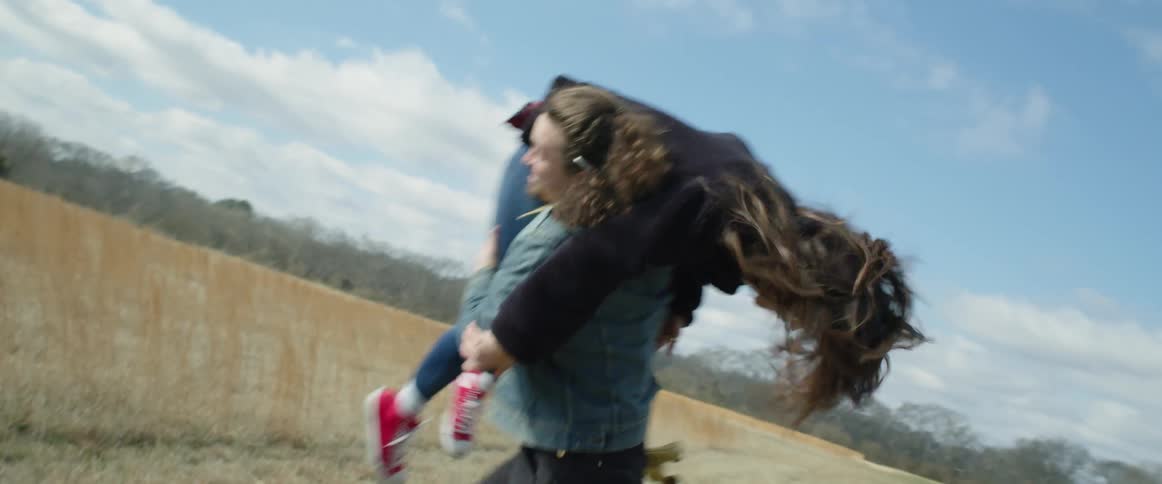 A teenage girl laughs as a boy picks her up and puts her over his shoulder and runs