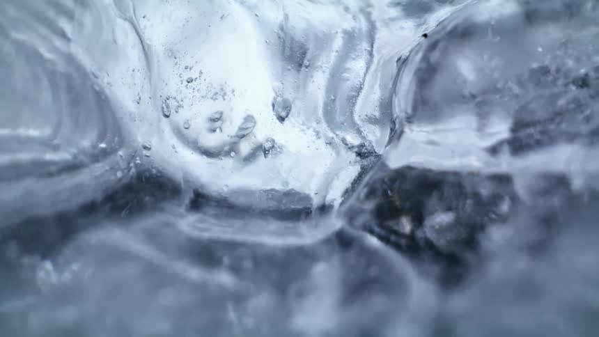Water drop dripping over a sheet of ice hanging near a waterfall at winter