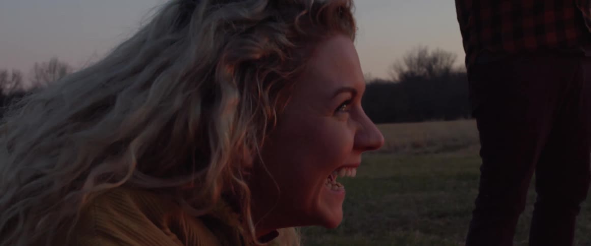 A young blonde woman giggles at what appears to be an outdoor gathering