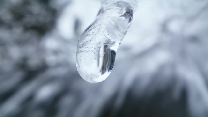 Close up of droplets of water melting off an icicle in front of a water fall