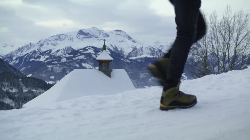 A person walks up a snowy mountain slope next to a church on a cloudy day