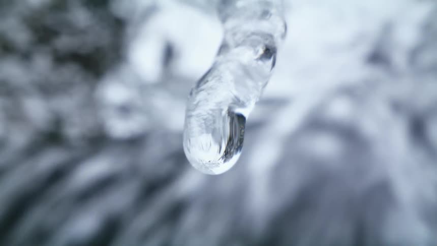Water drips from the end of a icicle onto a rushing river below