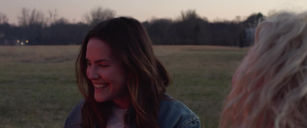 Two women are laughing and sitting outdoors at dusk