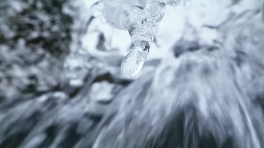 Water melts from a small icicle in front of a stream of water pouring downwards