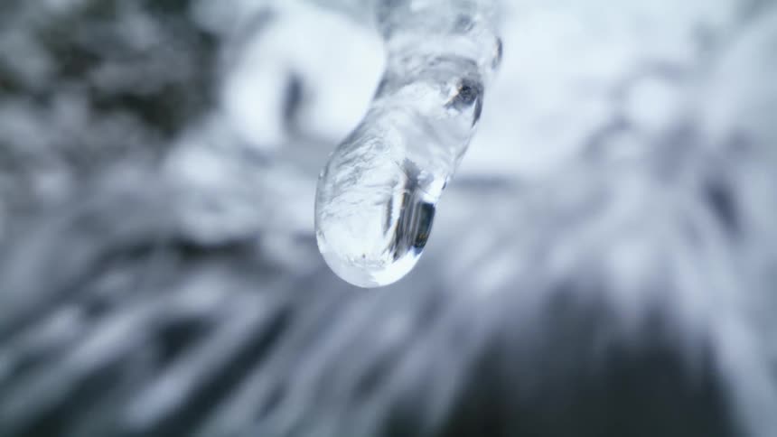 Water drops dripping from an icicle near a waterfall