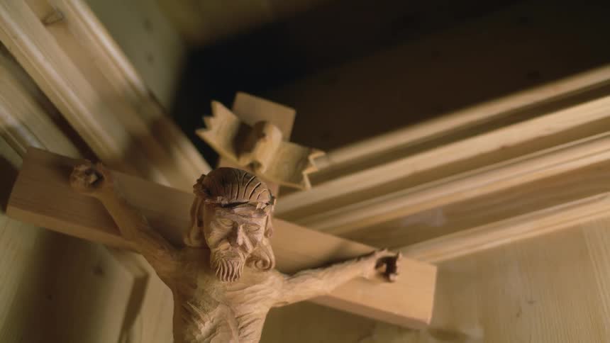 A crucifix with jesus on a cross hangs in the corner of a wall in a room