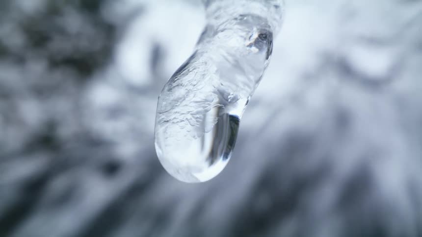 Water drop dripping from an icicle hanging near a waterfall at winter