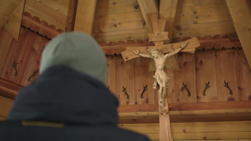 A person staring at a cross that is hanging on a wall in a church