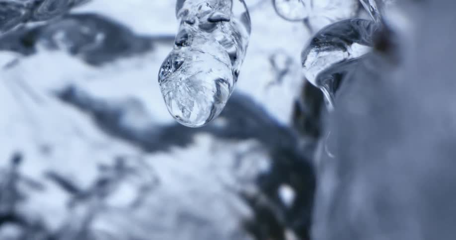 Water drop dripping from an icicle hanging near a waterfall at winter