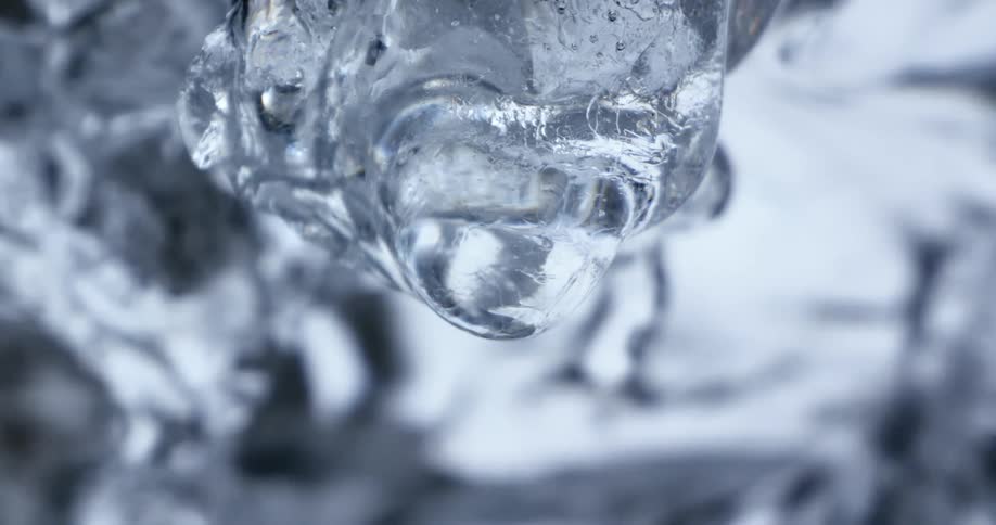 Water drop dripping from an icicle hanging near a waterfall at winter