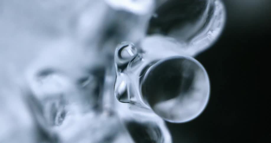 Water drop dripping from an icicle hanging near a waterfall at winter