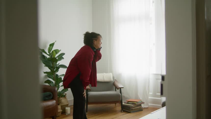 A woman laughs while talking on her smartphone in the living room of a house during the day