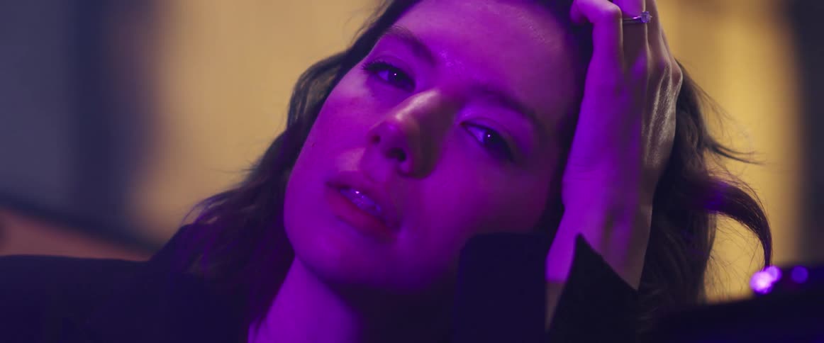 Woman sitting under purple light stares while holding head with hand