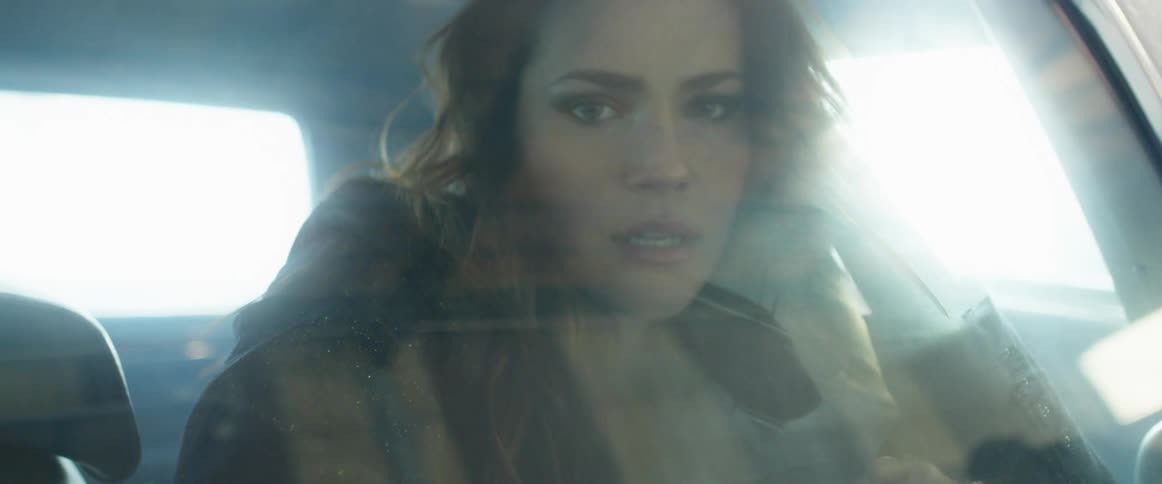 A woman in a vehicle staring and touching her hair with her hands