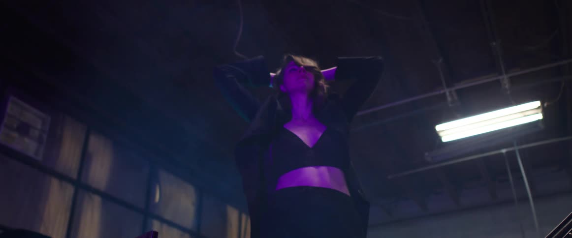 Young long haired woman inside a warehouse walks among the parked cars modeling for the camera