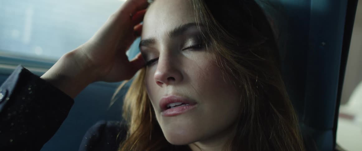 A woman sitting in a car runs her hand through her hair