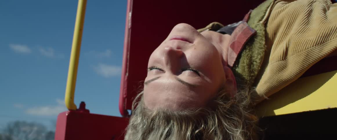 Long haired blonde woman resting upside down over a colorful structure outdoors