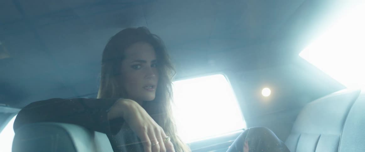A woman sitting in a vehicle and staring with her hand on her head