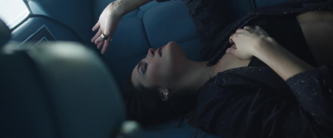 A woman laying down in the back seat of a vehicle and dancing to music