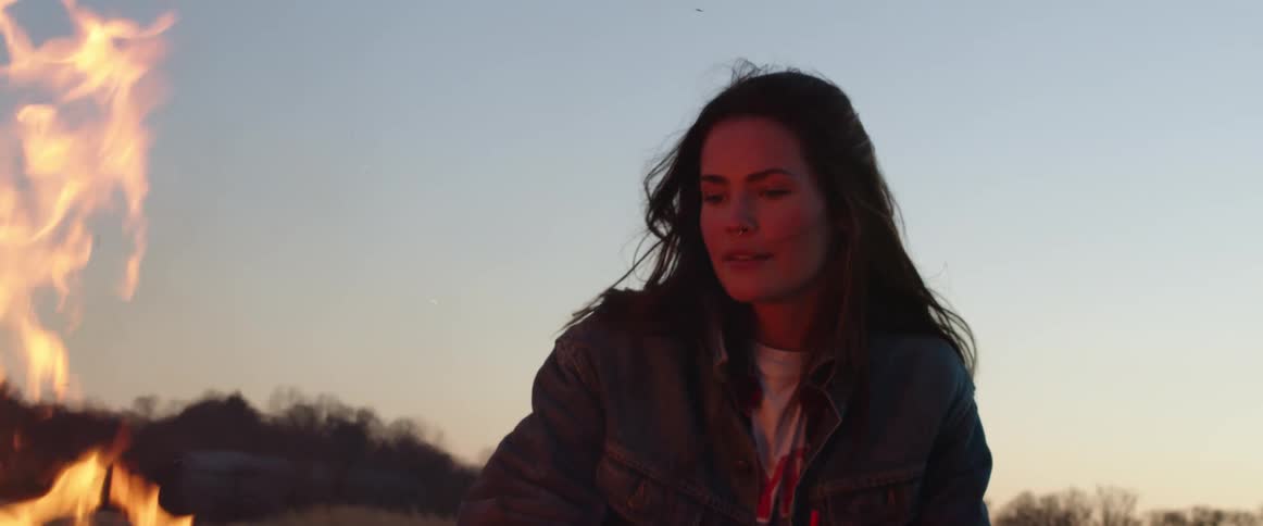 A woman is standing near the campfire