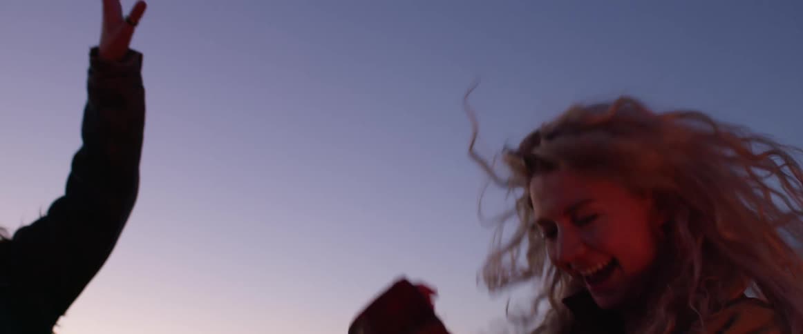 A woman holds a flask as she laughs and dances with friends at dusk