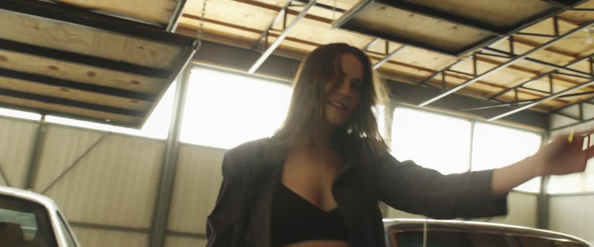 Young woman dancing and looking at the camera while modeling in a warehouse filled with parked cars