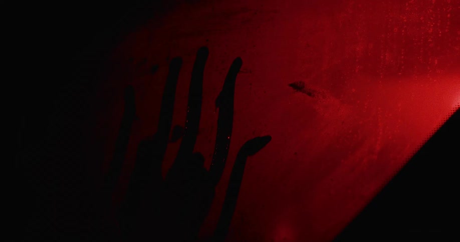 A person placing their hand on a foggy window with a red light in the background
