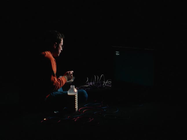 A man in a room sitting on the floor eating a bowl of cereal in front of a television