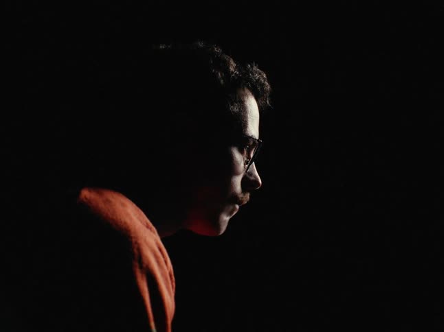 A man in an orange sweater eats cereal in a dark room