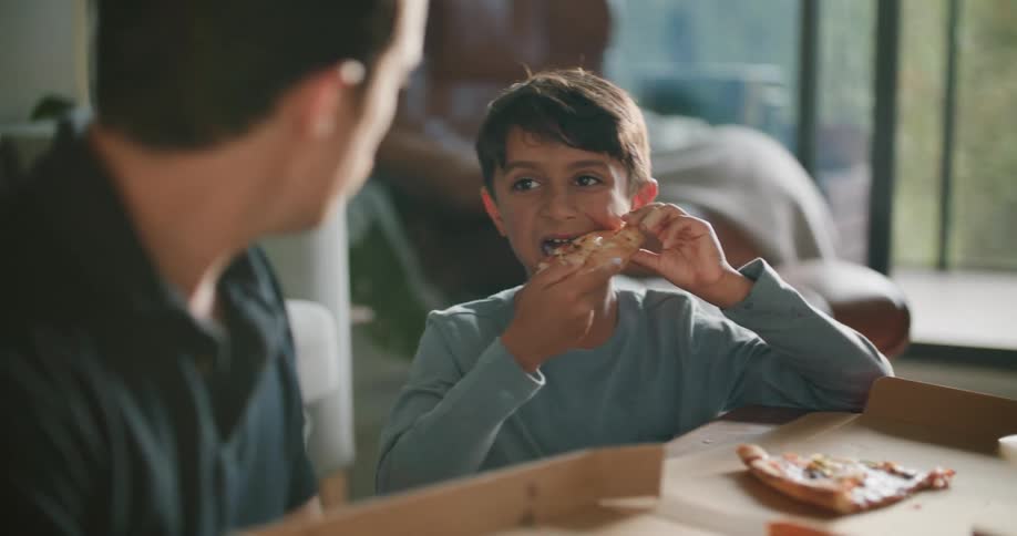 Father and son eating pizza sitting on the floor of the living room at home