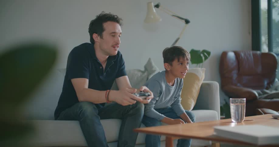 A young boy throws his arms in the air as he plays a video game with his father