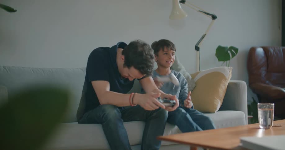 A man and a boy sitting on a couch next to a table holding videogame controllers