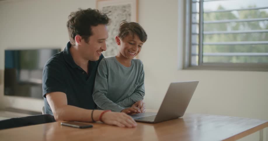 A father and son smiling and laughing while looking at a laptop screen