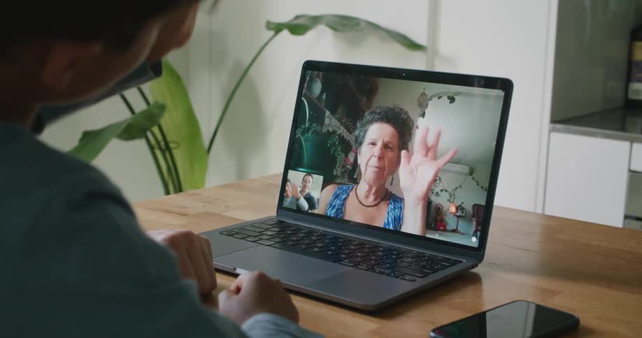 A grandma on a laptop screen blows kisses and waves at her son and grandson who are waving back