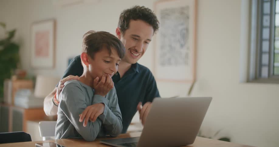 A man and a boy sitting next to a table with a laptop