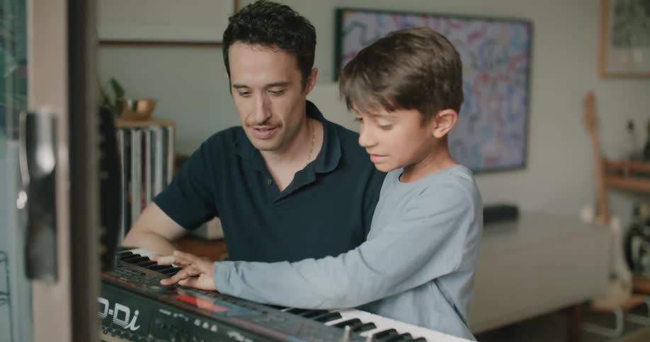 Father and son are playing the keyboard together indoors