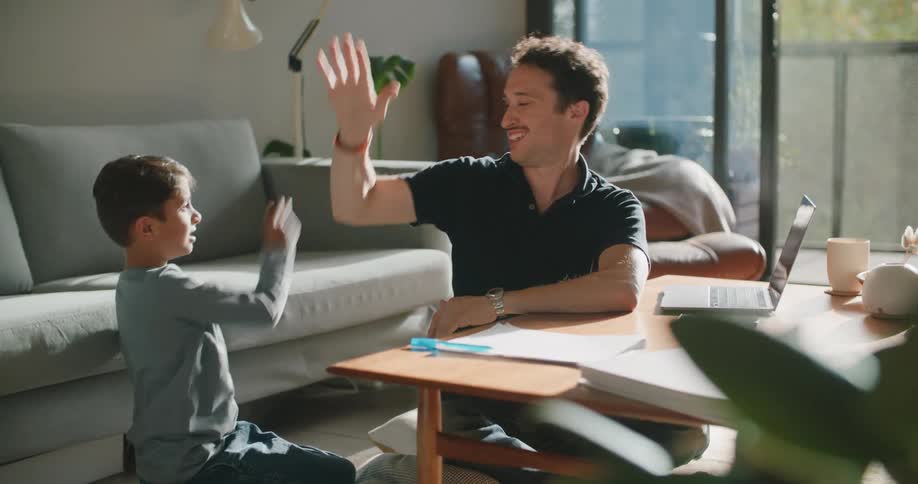 Father and son sitting at coffee table near laptop talk and high five each other