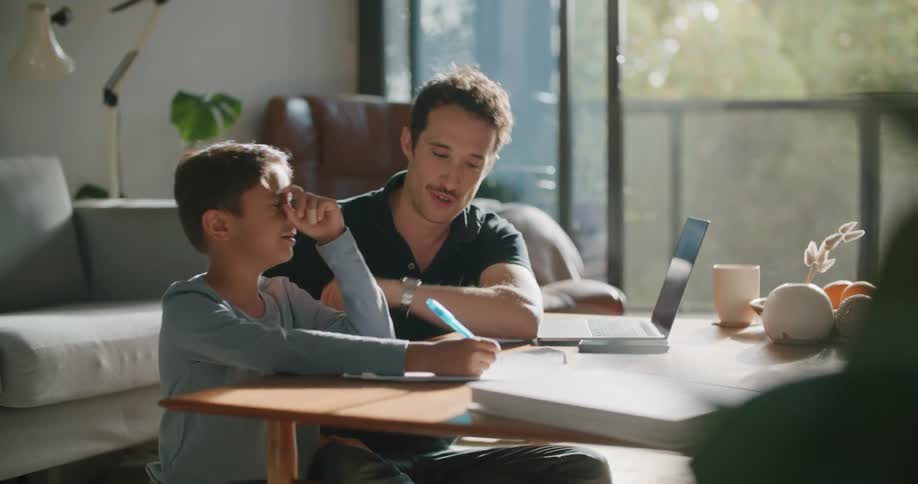 A man and a boy sitting on the floor next to a table with a laptop