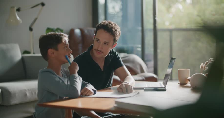 A father sits at home and helps his son with his school work