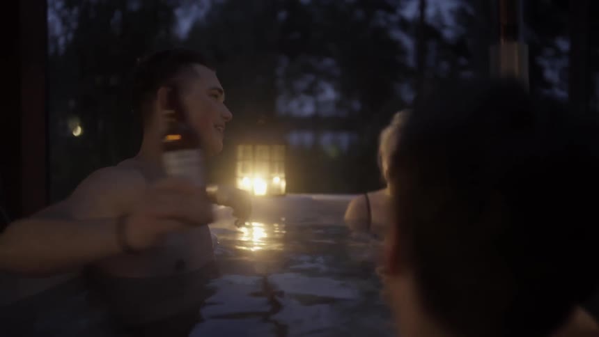 Friends have beers in a hot tub at night