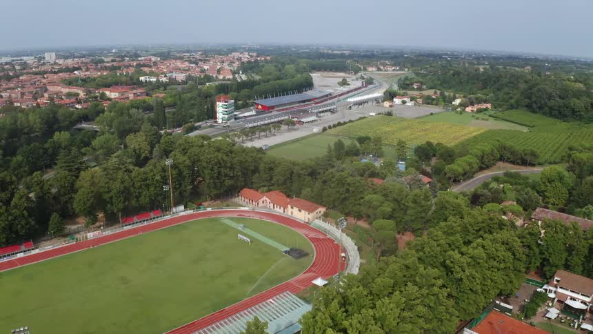 A town with a running track surrounded by trees with houses the sky and clouds in the background