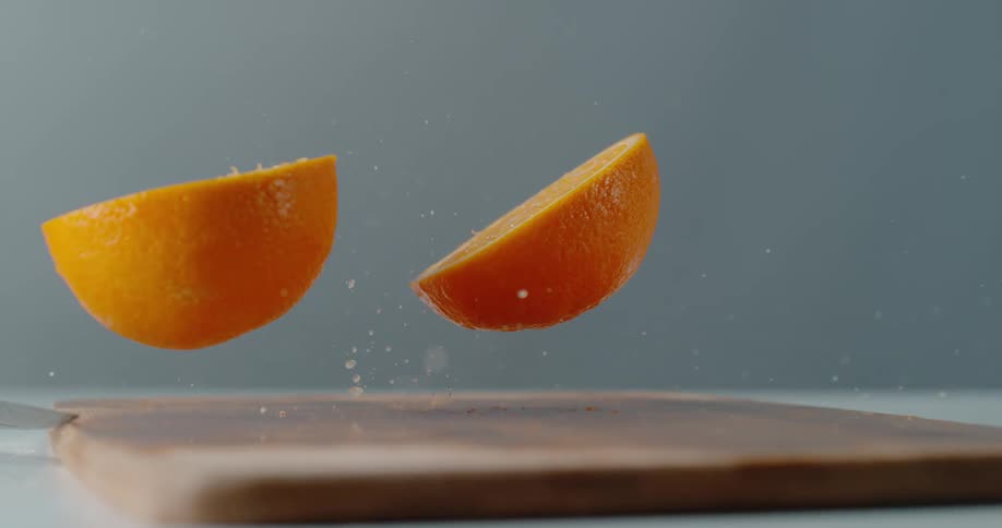 An orange falling and splitting on a cutting board