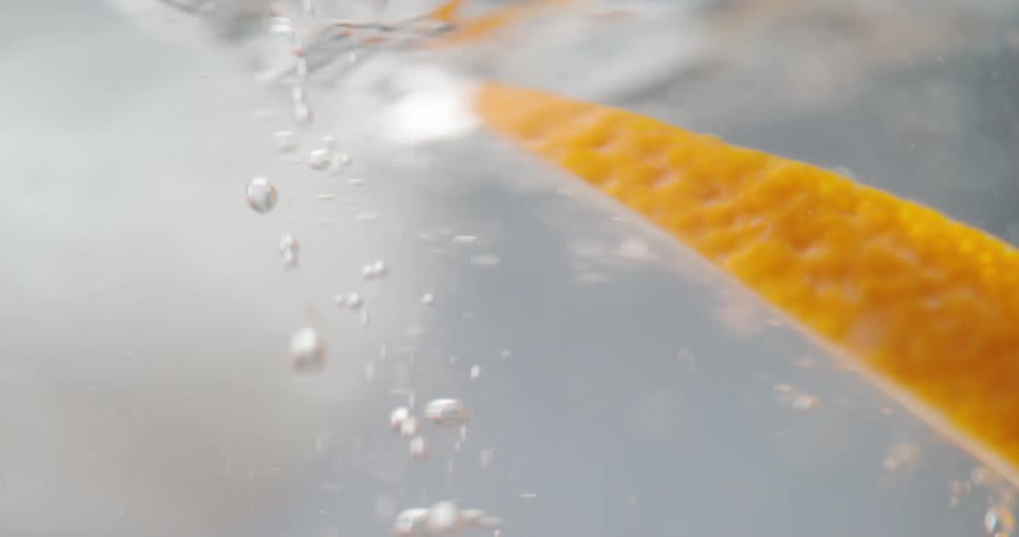 An orange slice falling into a glass of water
