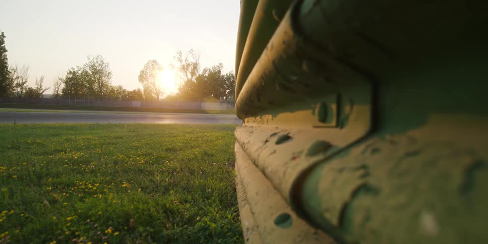 Guard rail with road nearby and a bright sun shining through the trees