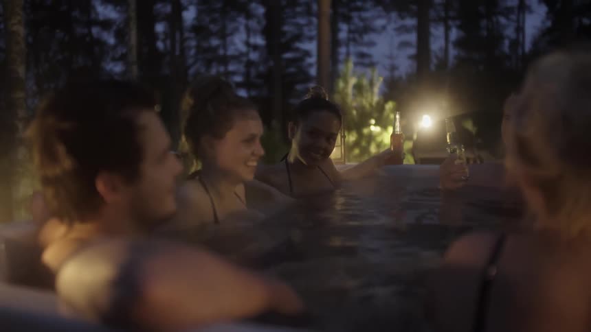 People sitting in a hot tub chatting and drinking beer as night falls
