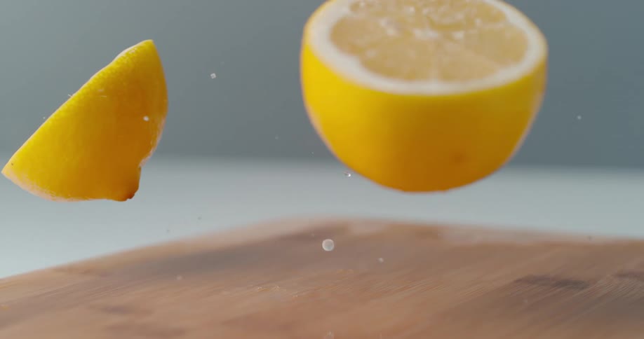 Two half of a lemon split as the lemon bounces against the surface of a wooden cutting board