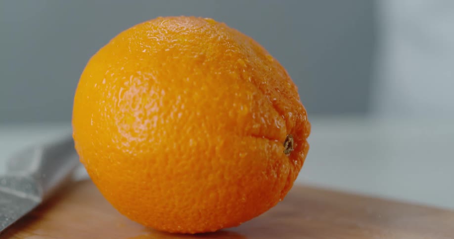 Orange drops onto chopping board bouncing and shedding water droplets
