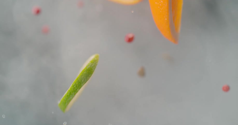 Slices of citrus fruit and water droplets fly upward through thick mist